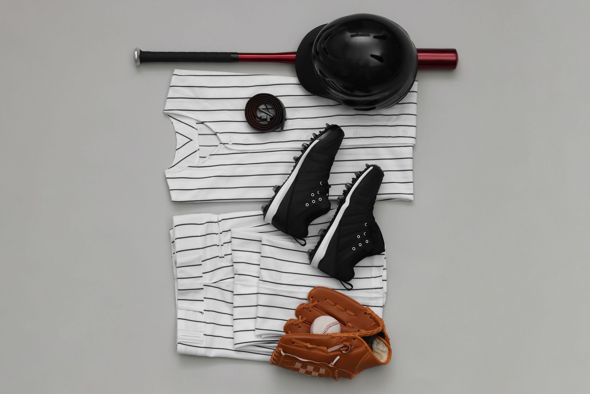 Baseball uniform and other sports equipment on white background, flat lay