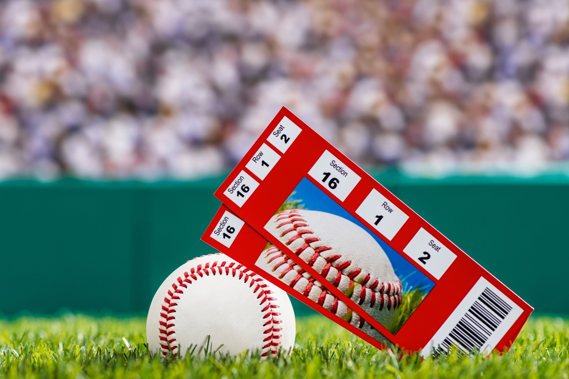 A pair of ticket stubs sitting on a baseball in the grass of a stadium